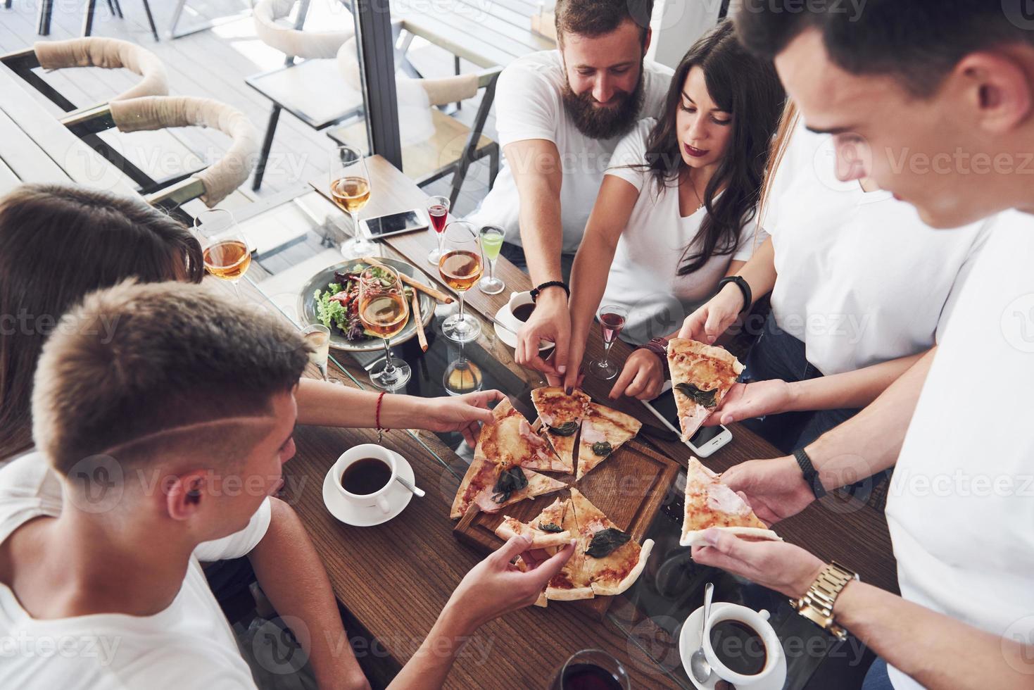 Tasty pizza on the table, with a group of young smiling people resting in the pub photo