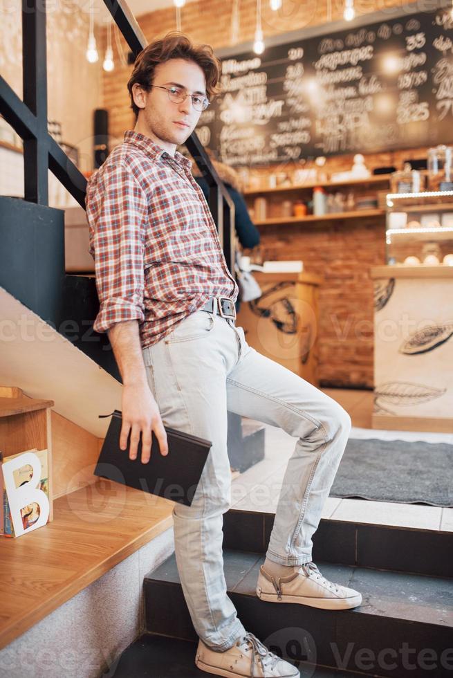 Talented young man in casual shirt drawing sketch in notebook enjoying leisure time in coffee shop.Skilled student writing down homework in notepad sitting in coworking photo