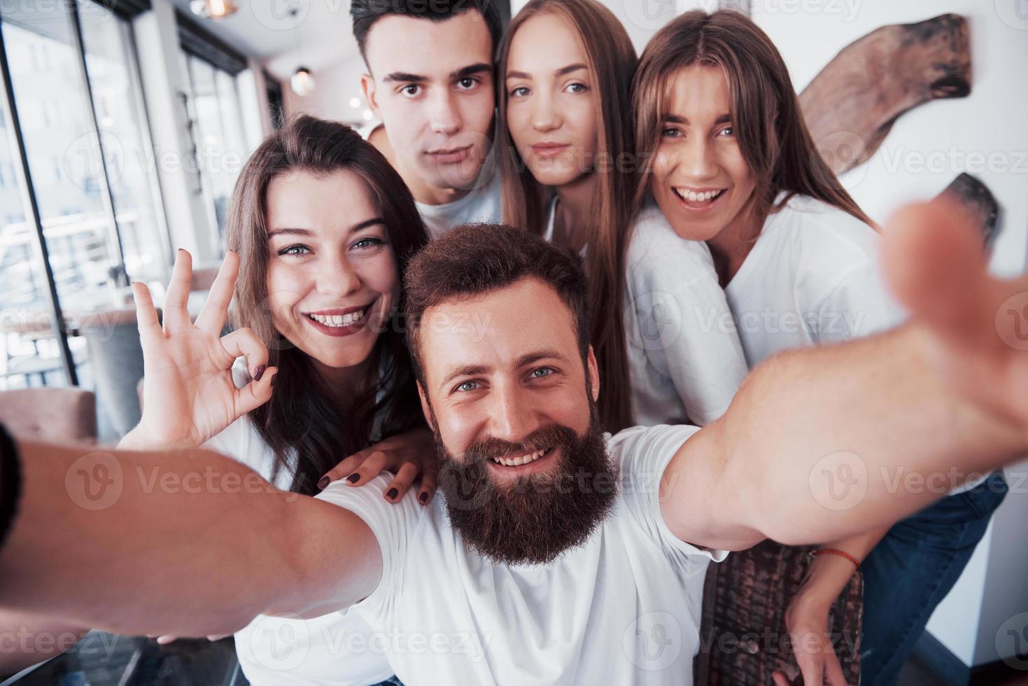 A group of people make a selfie photo in a cafe. The best friends gathered together at a dinner table eating pizza and singing various drinks