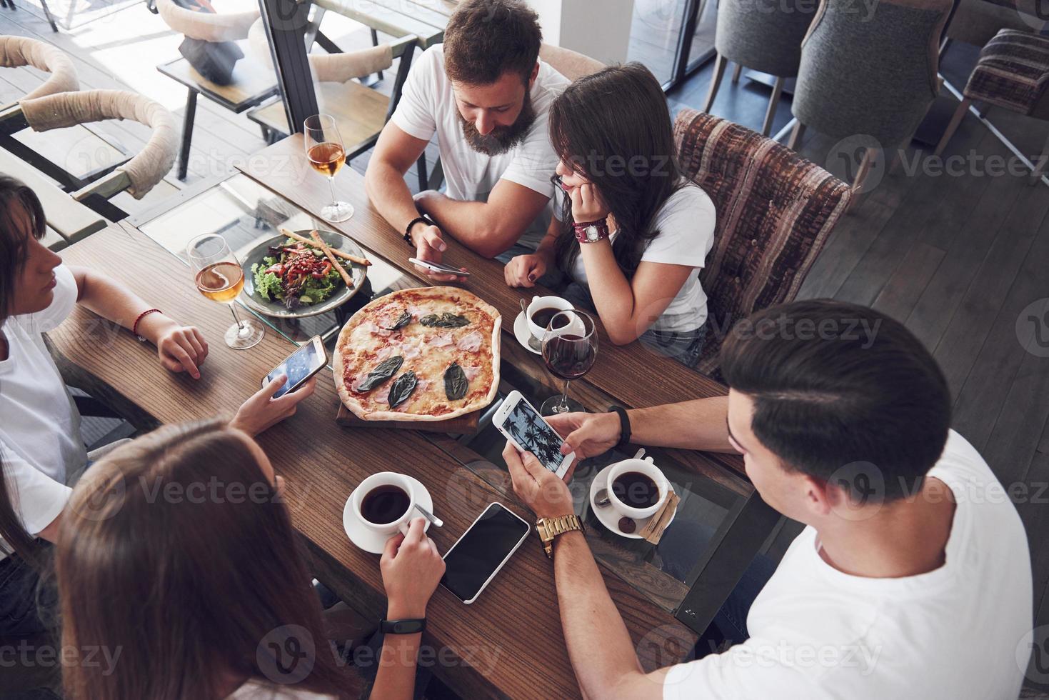 Tasty pizza on the table, with a group of young smiling people resting in the pub photo