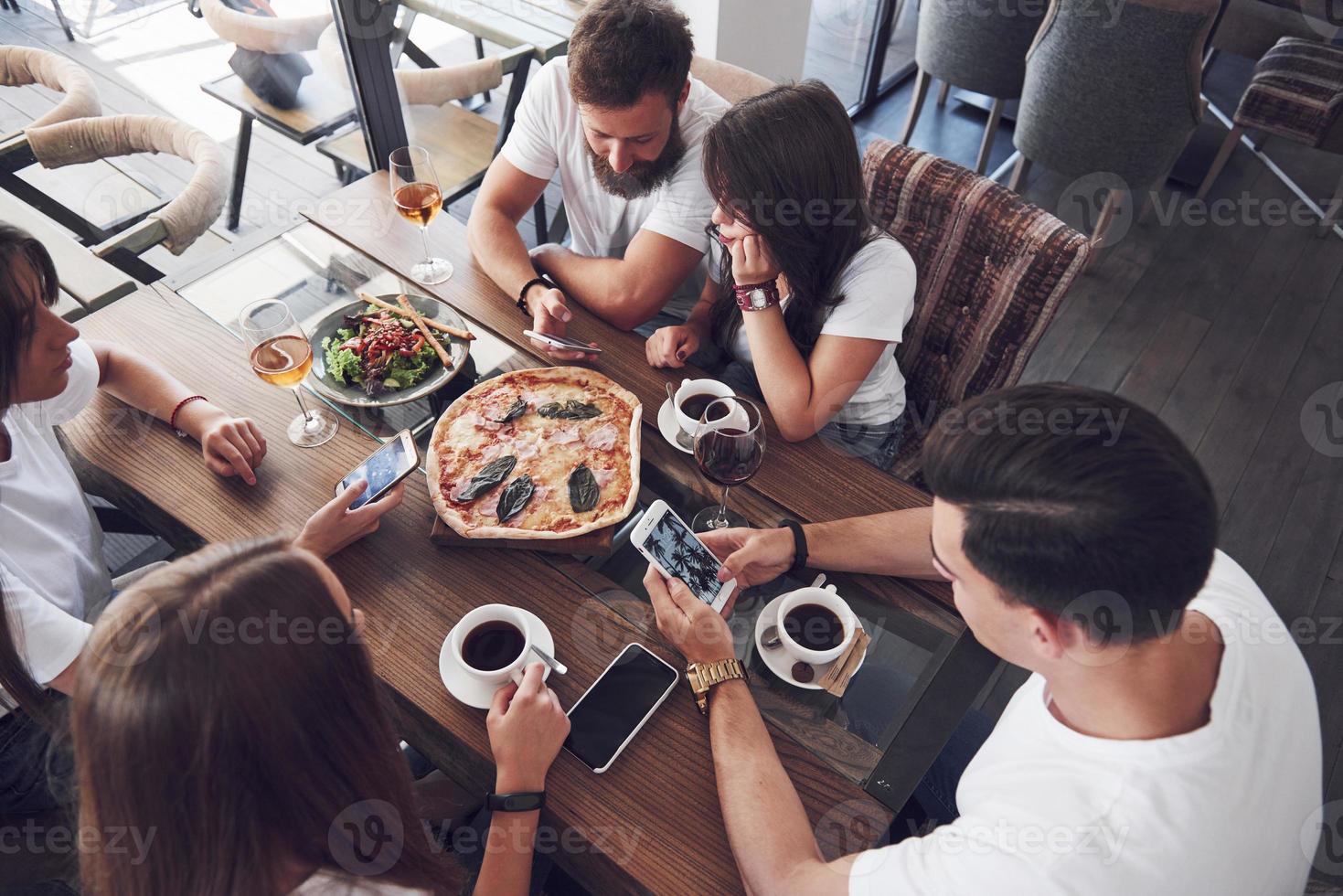 Sabrosa pizza en la mesa, con un grupo de jóvenes sonrientes descansando en el pub foto