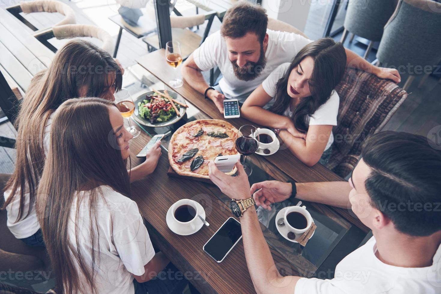 Tasty pizza on the table, with a group of young smiling people resting in the pub photo