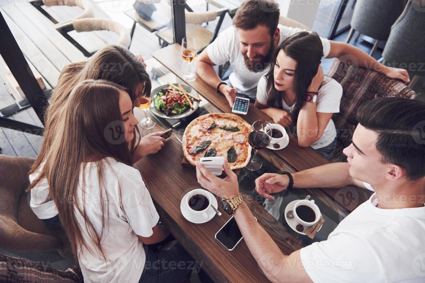 Sabrosa pizza en la mesa, con un grupo de jóvenes sonrientes descansando en el pub foto