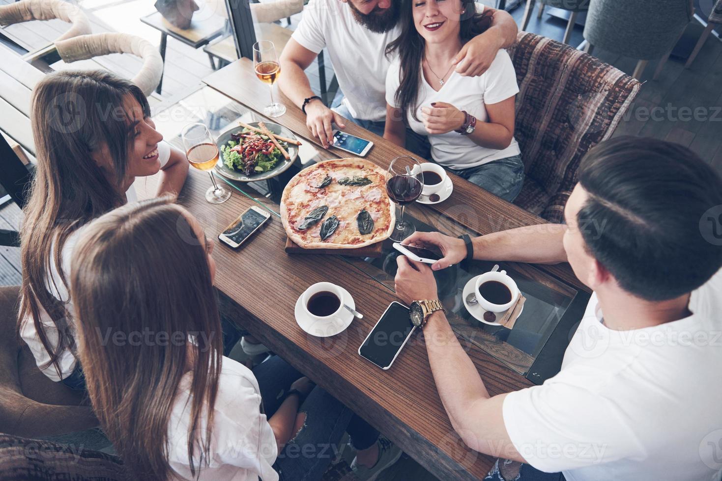 Tasty pizza on the table, with a group of young smiling people resting in the pub photo