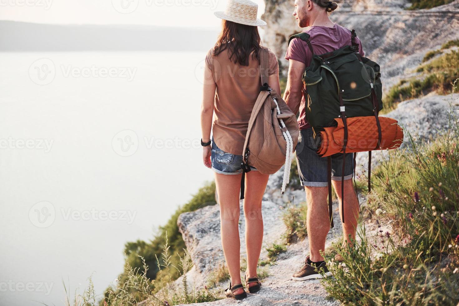 Two tourist male and woman with backpacks stand to the top of the mountain and enjoying sunrise. Travel lifestyle adventure vacations concept photo
