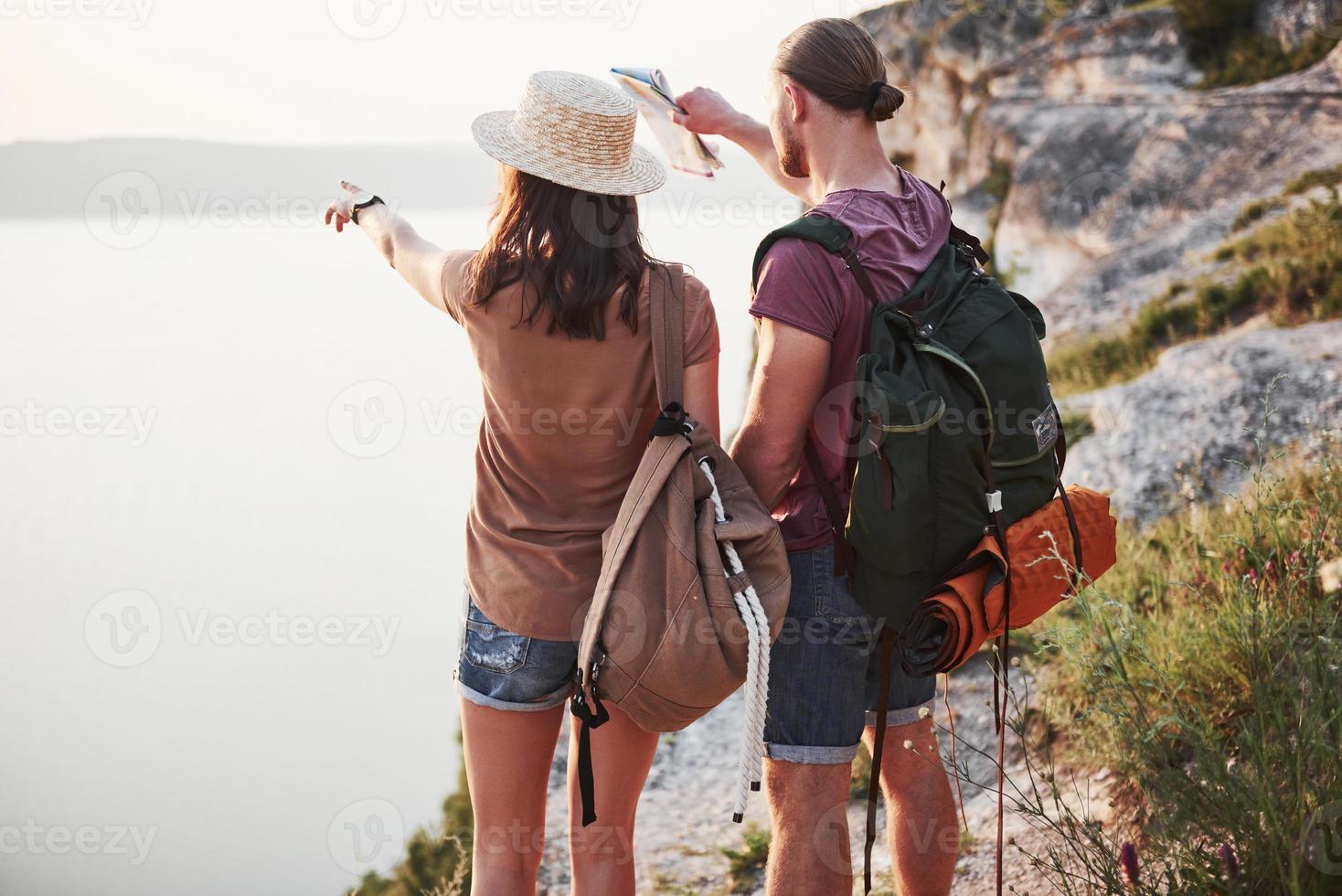 Two tourist male and woman with backpacks stand to the top of the crag and enjoying sunrise. Traveling mountains and coast, freedom and active lifestyle concept photo