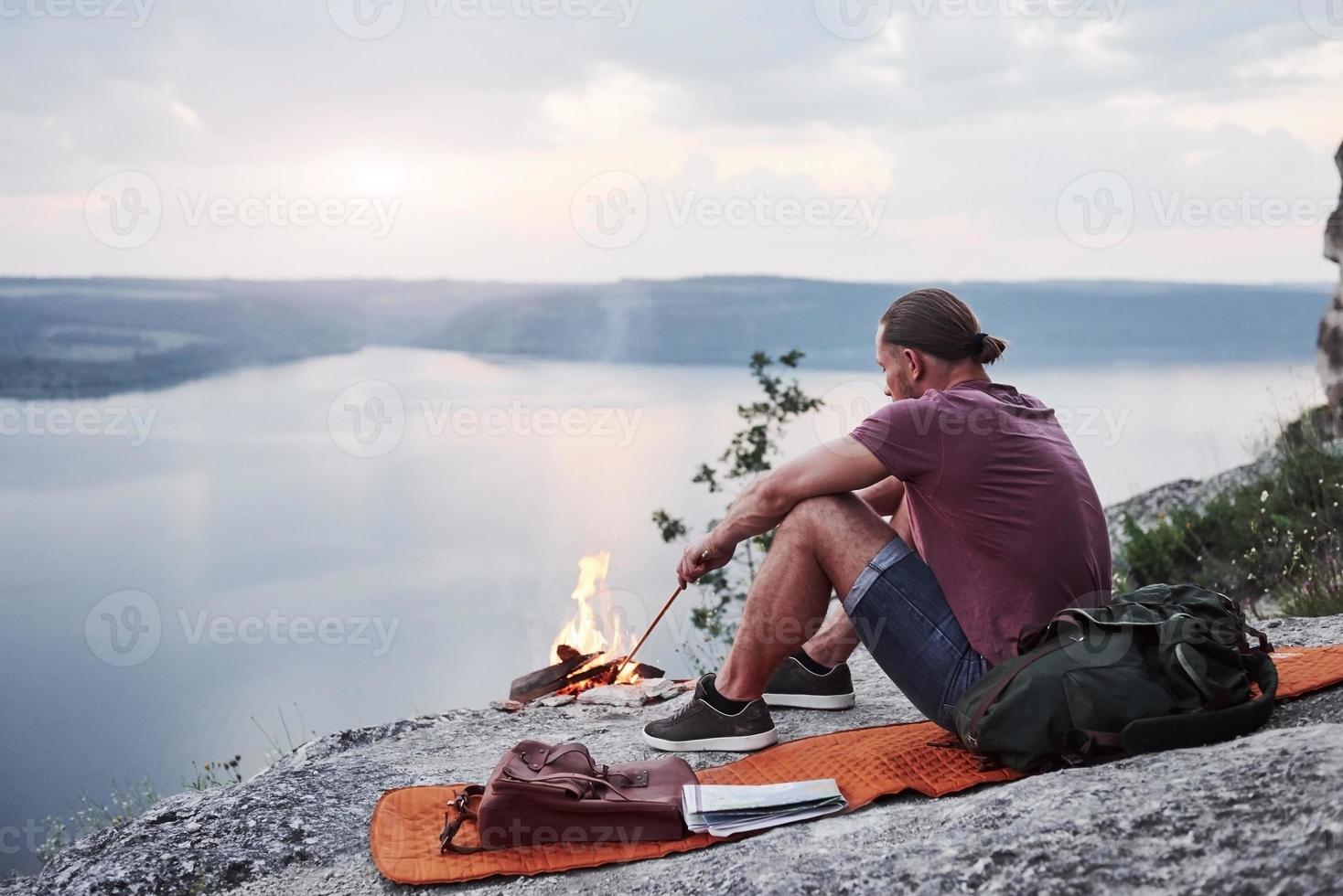 excursionista hombre exitoso en la cima de la roca con fogata. viajando a lo largo de las montañas y la costa, la libertad y el concepto de estilo de vida activo foto