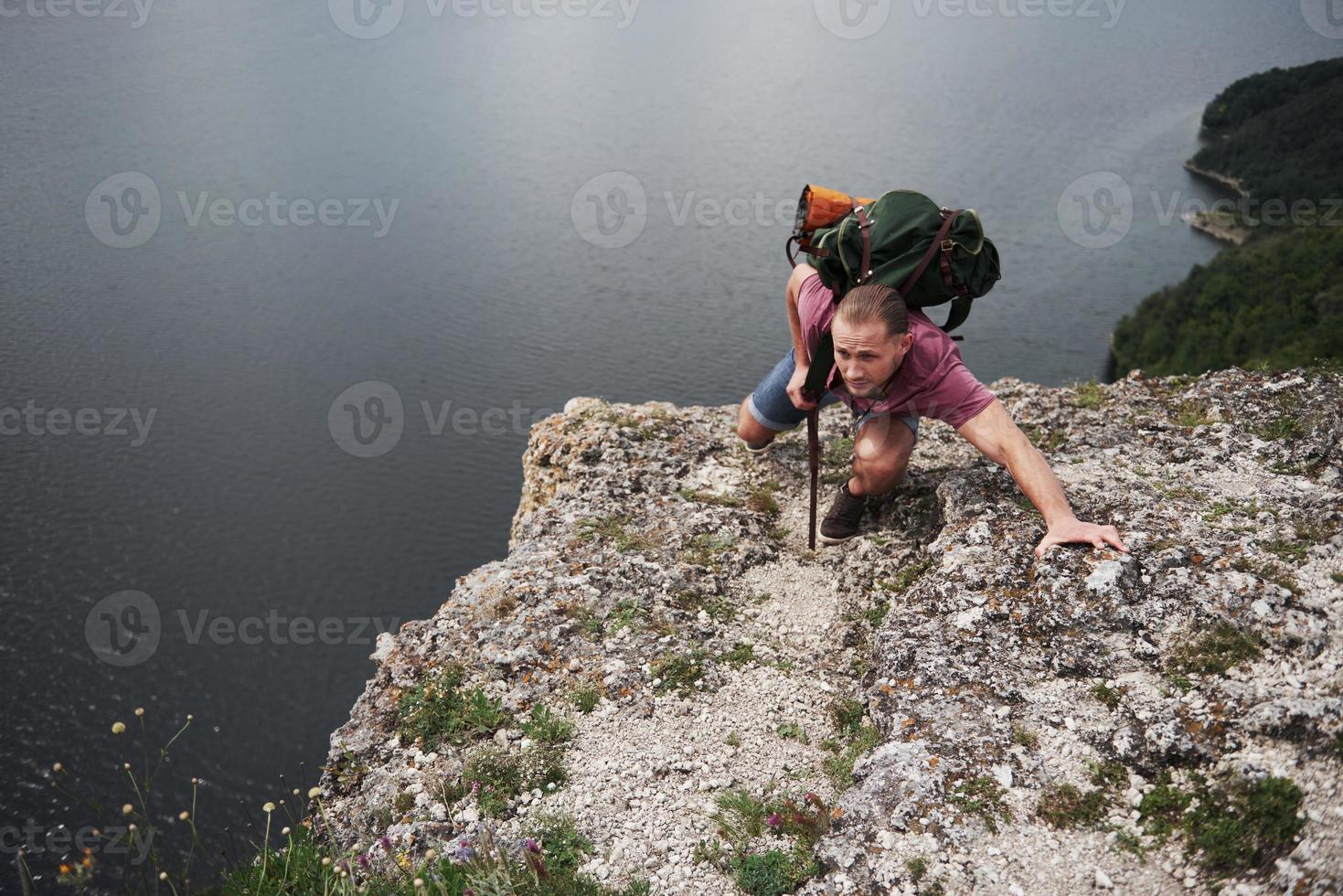 Traveller with backpack sitting on top of mountain enjoying view above the water surface. Traveling along mountains and coast, freedom and active lifestyle concept photo