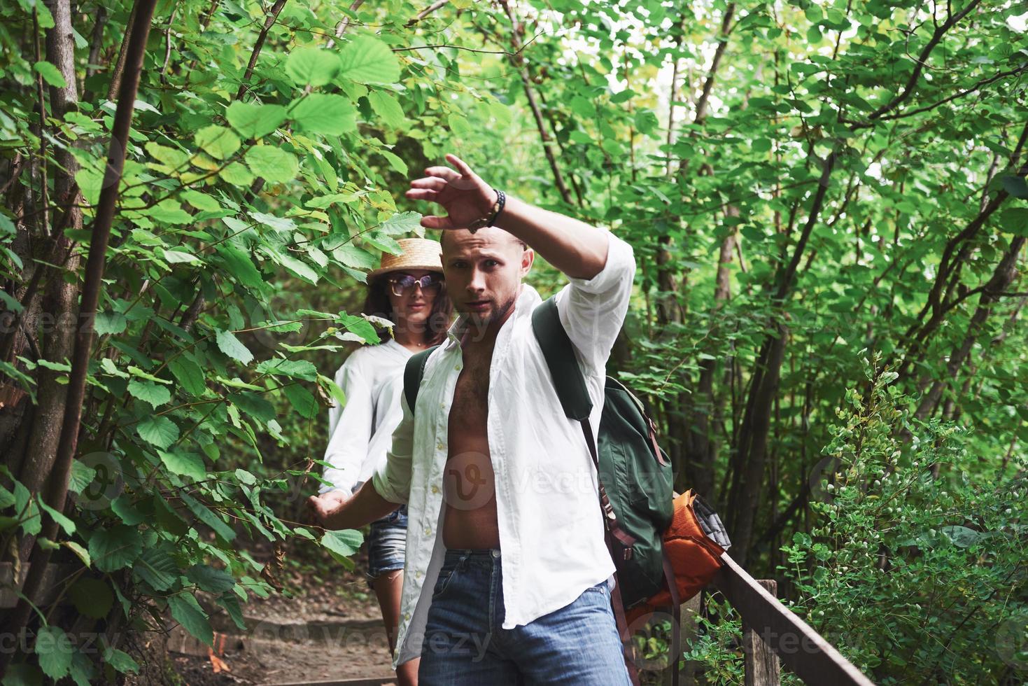 Two hikers with backpacks on the back in nature. Man and woman holding hands while walk on a summer day photo