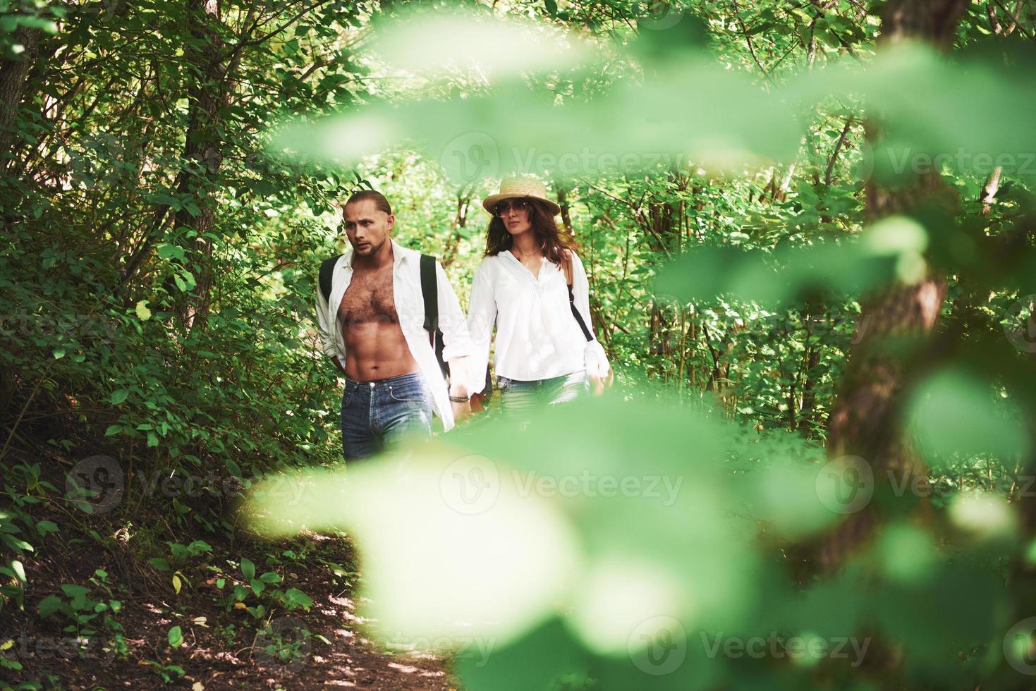 Two hikers with backpacks on the back in nature. Young couple man and woman like an active holiday with a tent, so they got out on the nature in a sunny day photo