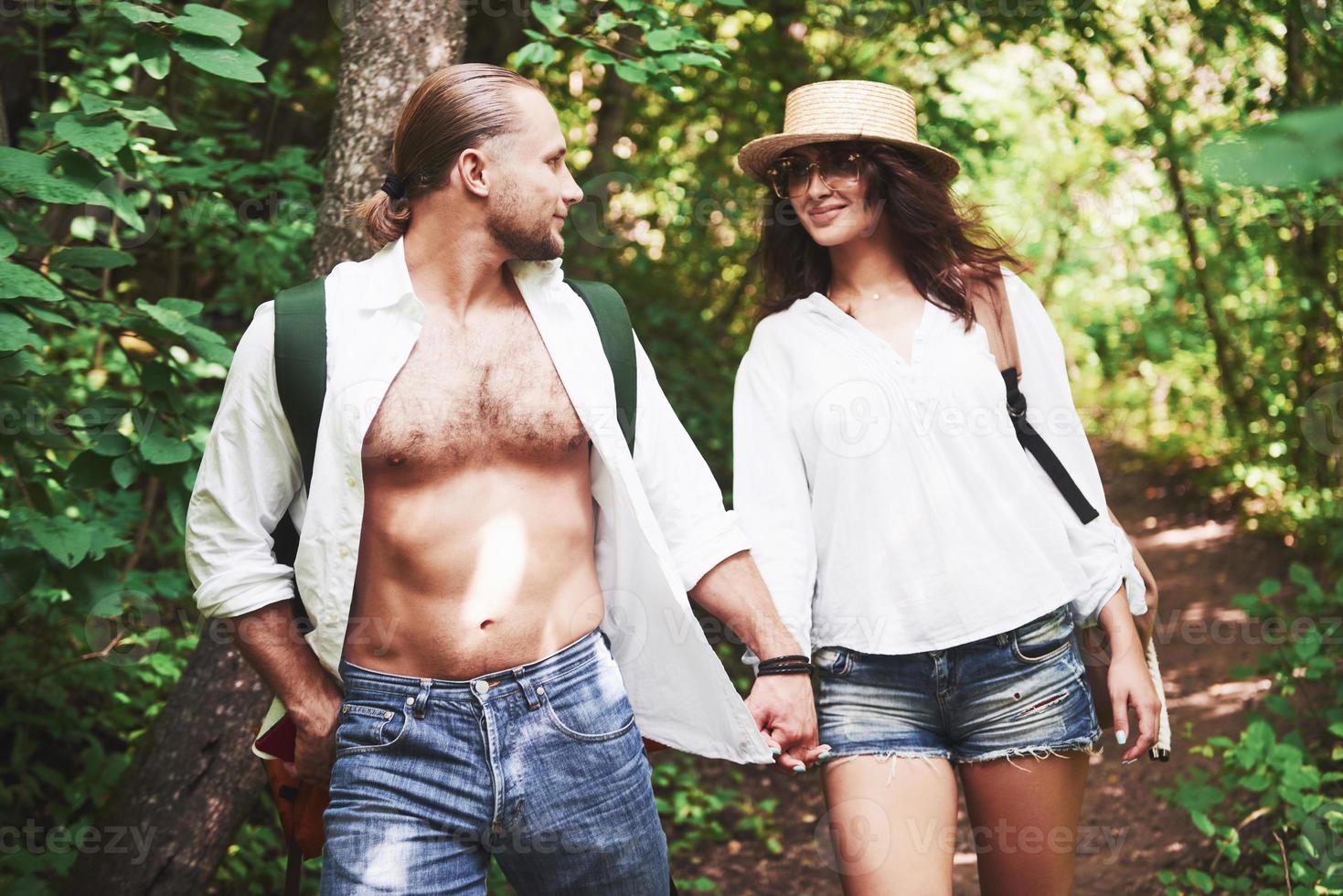 Two hikers with backpacks on the back in nature. Man and woman holding hands while walk on a summer day photo