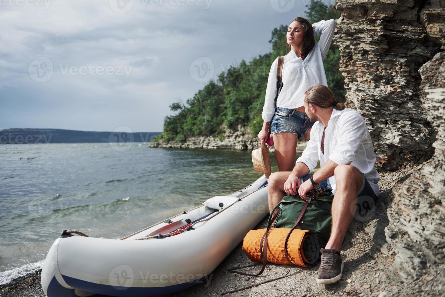 Cute young and couple on river background. A guy and a girl with backpacks are traveling by boat. Traveler summer concept photo