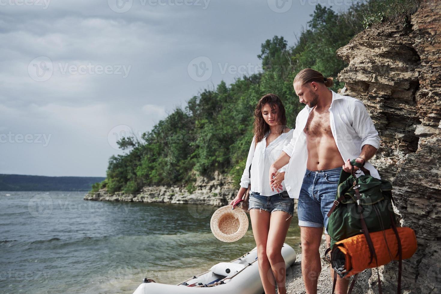 lindo joven y pareja en el fondo del río. un chico y una chica con mochilas viajan en barco. concepto de verano viajero foto