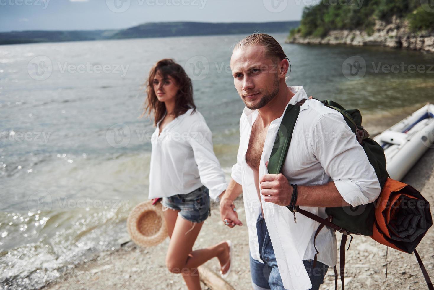 lindo joven y pareja en el fondo del río. un chico y una chica con mochilas viajan en barco. concepto de verano viajero foto