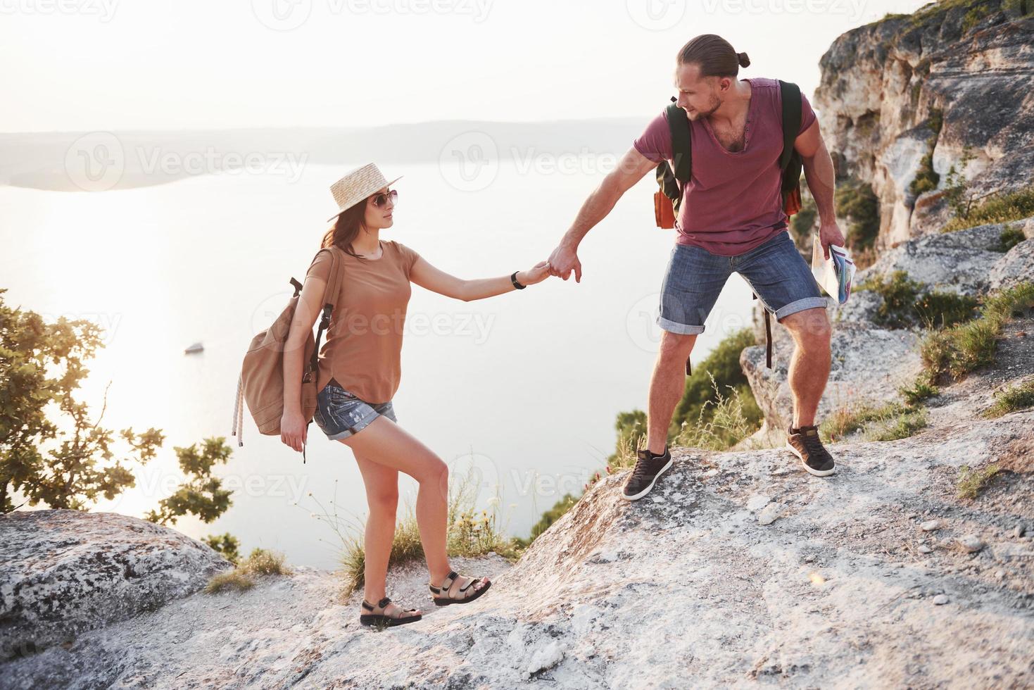 Two tourist male and woman with backpacks climb to the top of the mountain and enjoying sunrise. Travel lifestyle adventure vacations concept photo