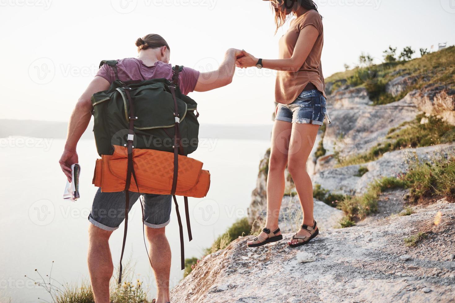 Two tourist male and woman with backpacks climb to the top of the mountain and enjoying sunrise. Travel lifestyle adventure vacations concept photo