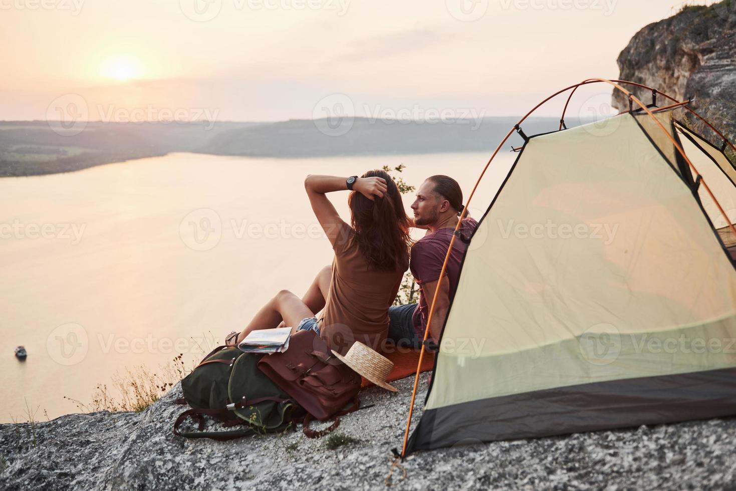 Photo of happy couple sitting in tent with a view of lake during hiking trip. Travel Lifestyle adventure vacations concept