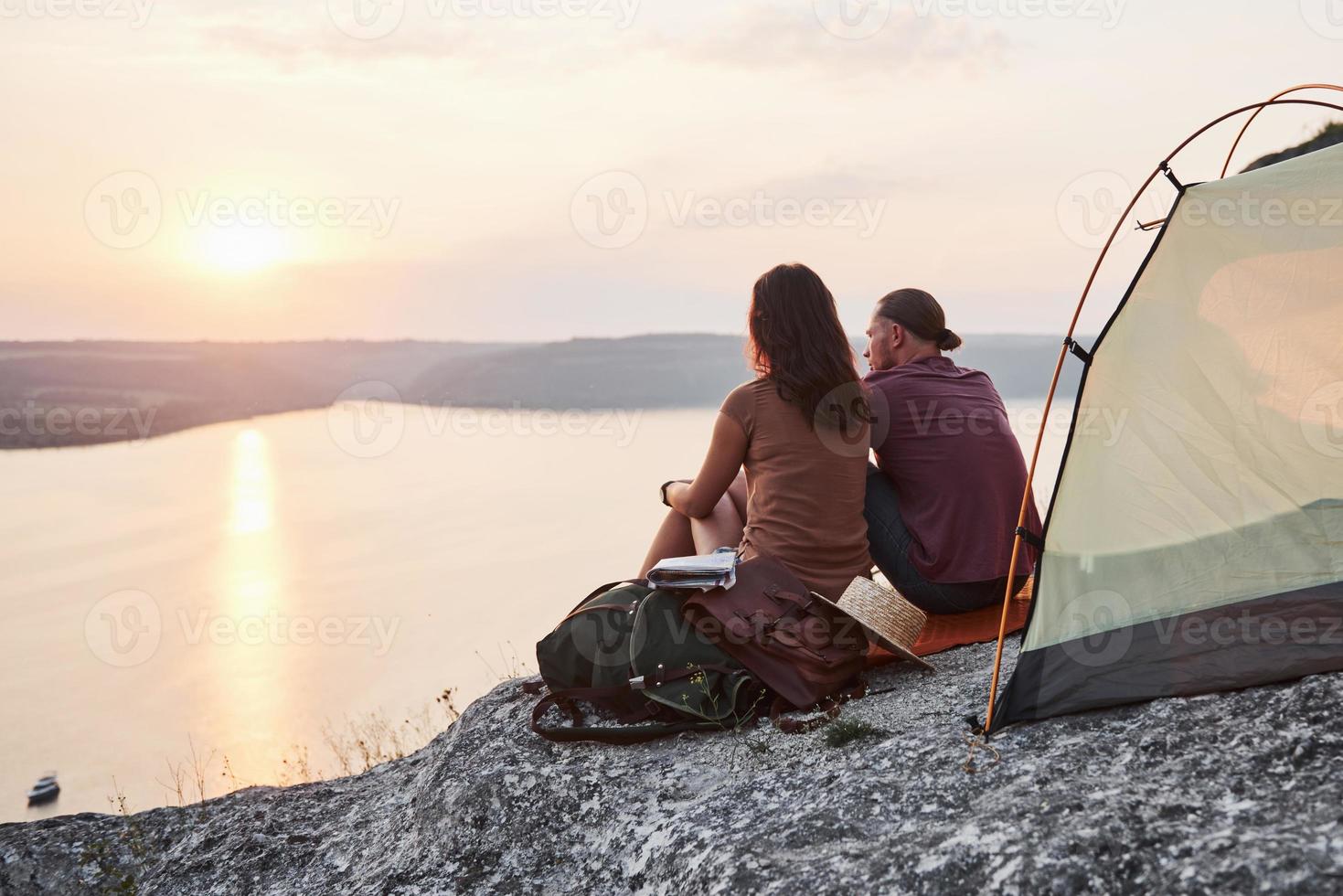 Photo of happy couple sitting in tent with a view of lake during hiking trip. Travel Lifestyle adventure vacations concept