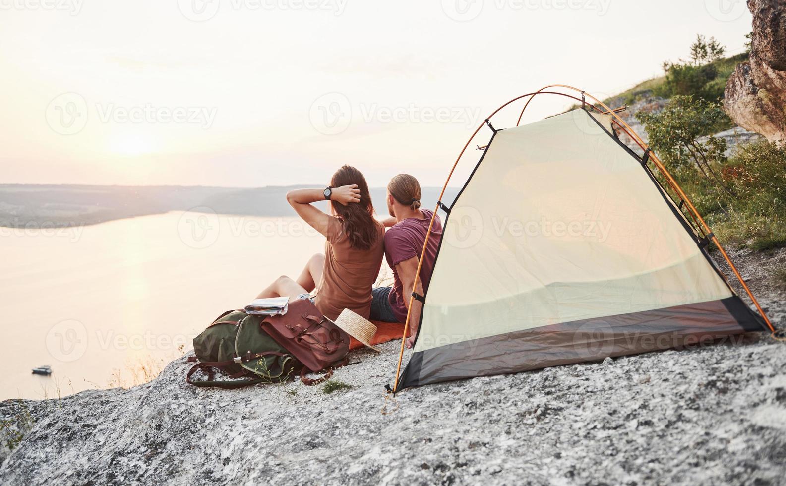 Photo of happy couple sitting in tent with a view of lake during hiking trip. Travel Lifestyle adventure vacations concept