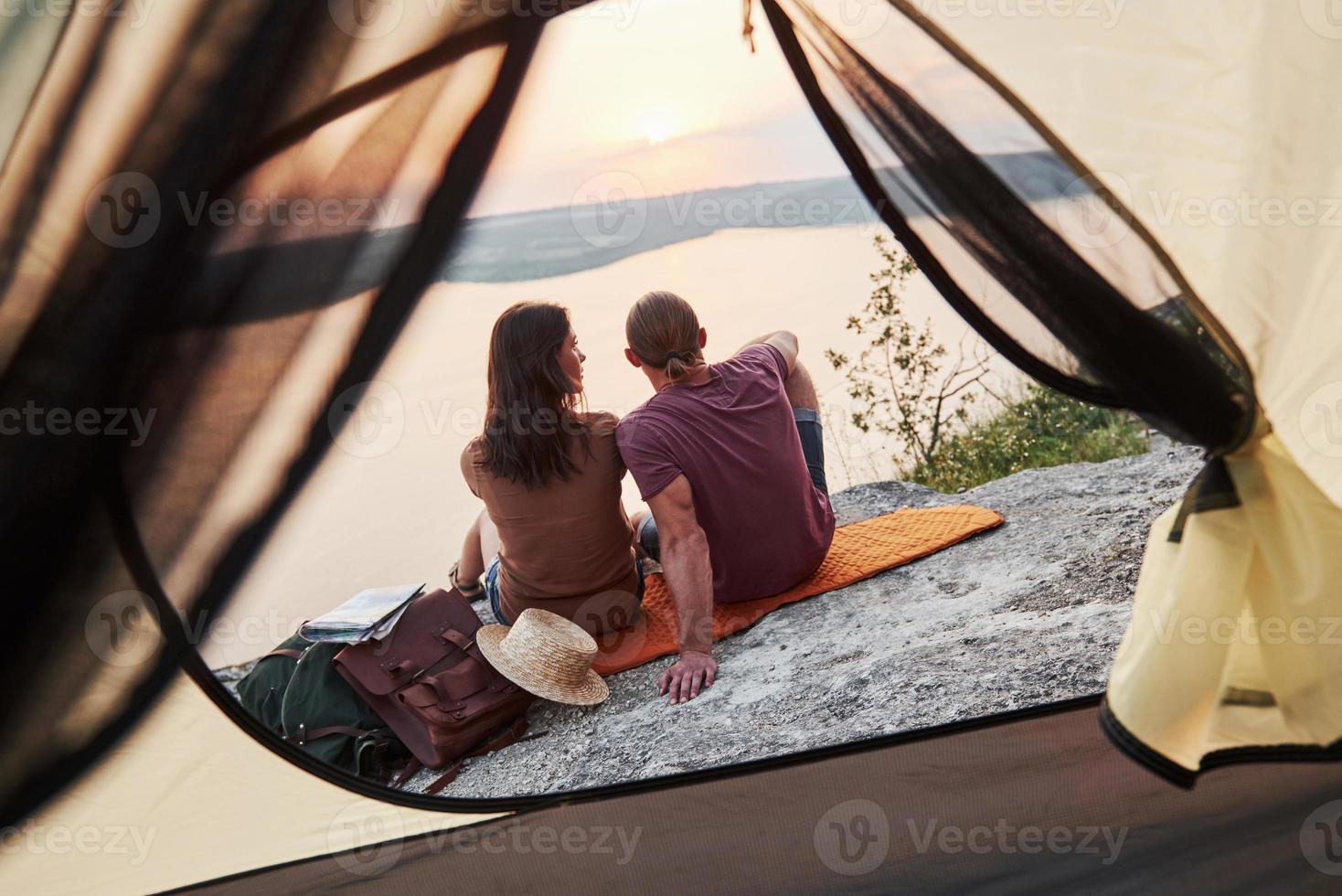 Photo of happy couple sitting in tent with a view of lake during hiking trip. Travel Lifestyle adventure vacations concept