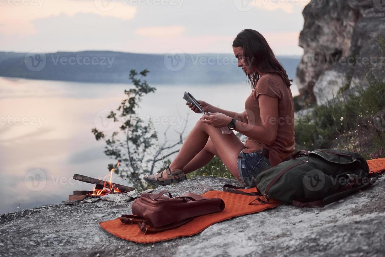 Hipster young girl with backpack enjoying sunset on peak of rock mountain. Tourist traveler on background view mockup photo