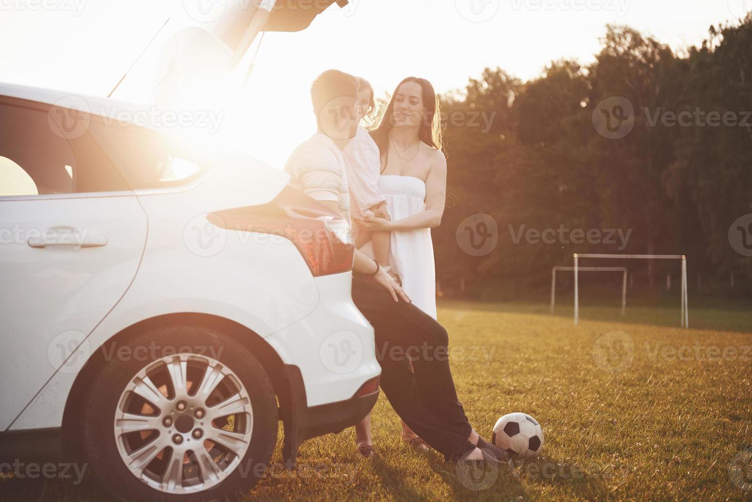 el abuelo y la abuela se sientan juntos en la naturaleza cerca del automóvil. hacen una foto selfie y su nieta juega con ellos.