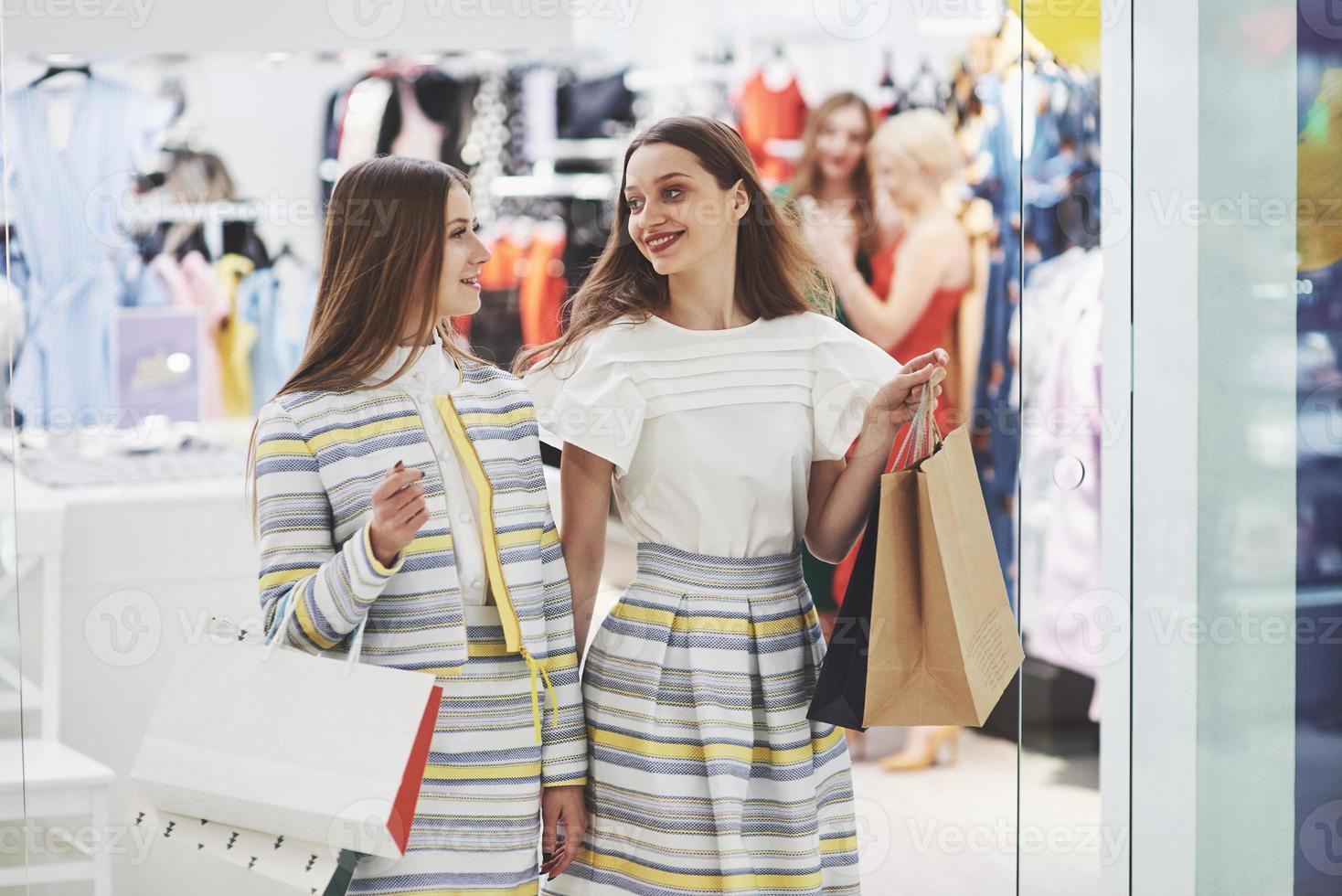 gran día para ir de compras. Dos hermosas mujeres con bolsas mirando el uno al otro con una sonrisa mientras camina en la tienda de ropa foto
