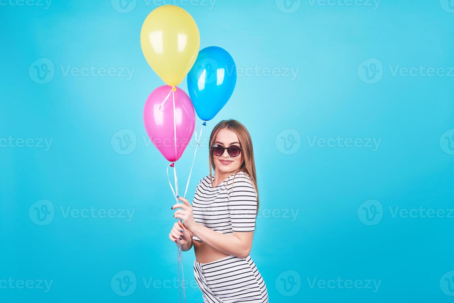 Feliz mujer sonriente está mirando en un aire globos de colores divirtiéndose sobre un fondo azul. foto