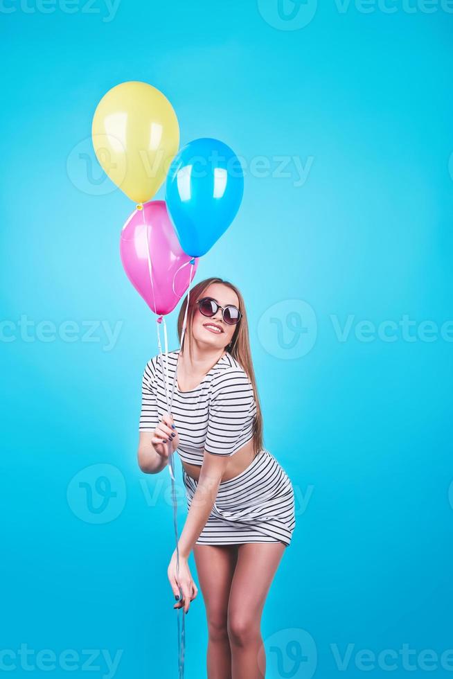 Happy smiling woman is looking on an air colorful balloons having fun over a blue background photo