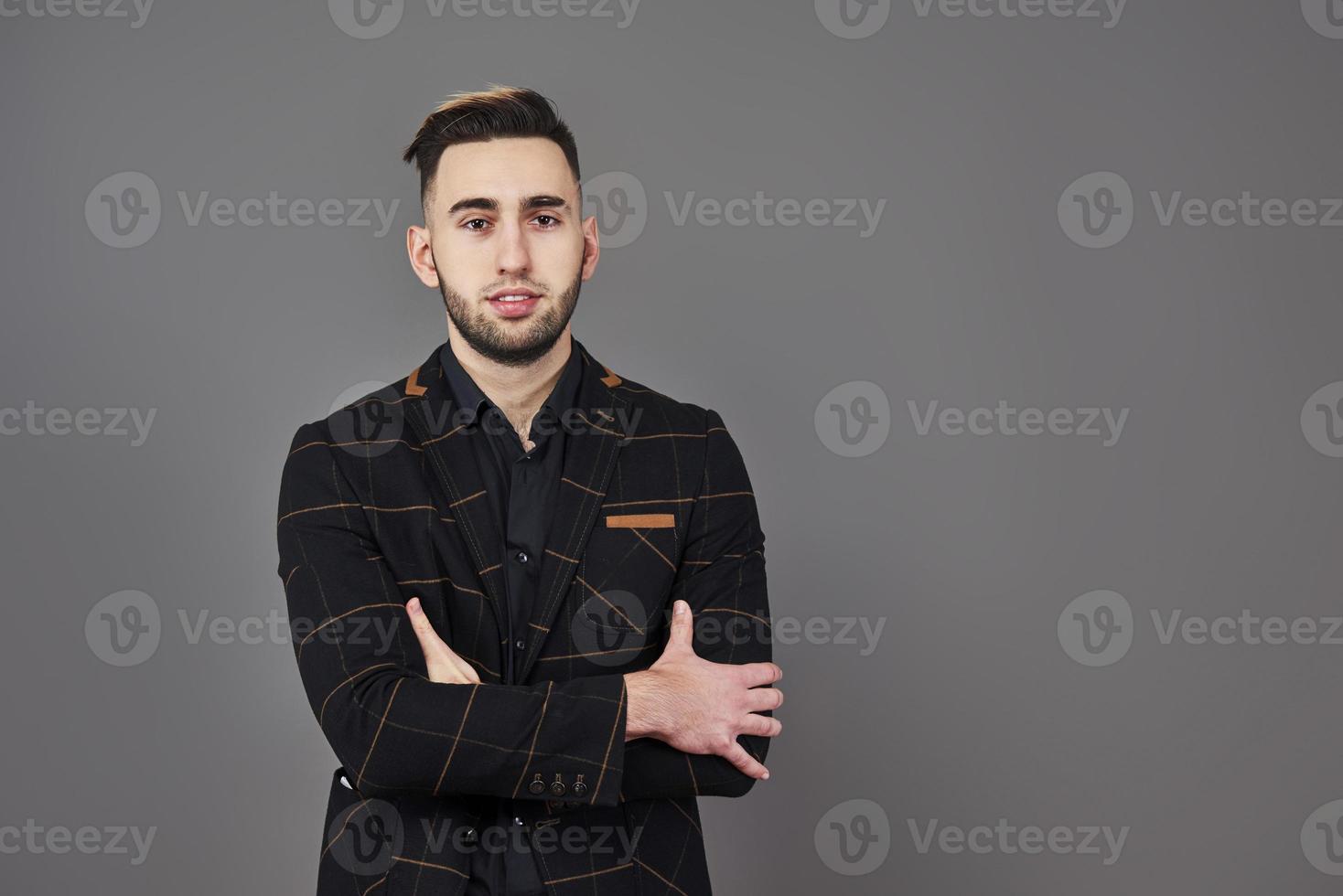 Exitoso joven empresario con un traje marrón con una hermosa sonrisa genuina posando sobre un fondo gris oscuro con espacio de copia foto