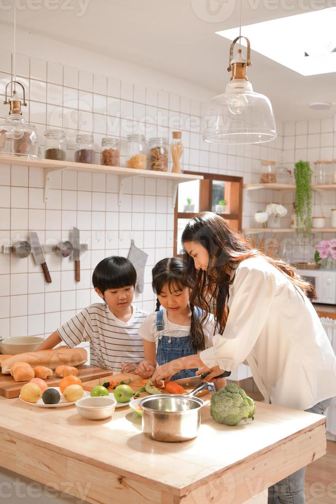 Momentos felices familiares cuando los niños ayudan a mamá a cocinar la comida en la cocina. foto