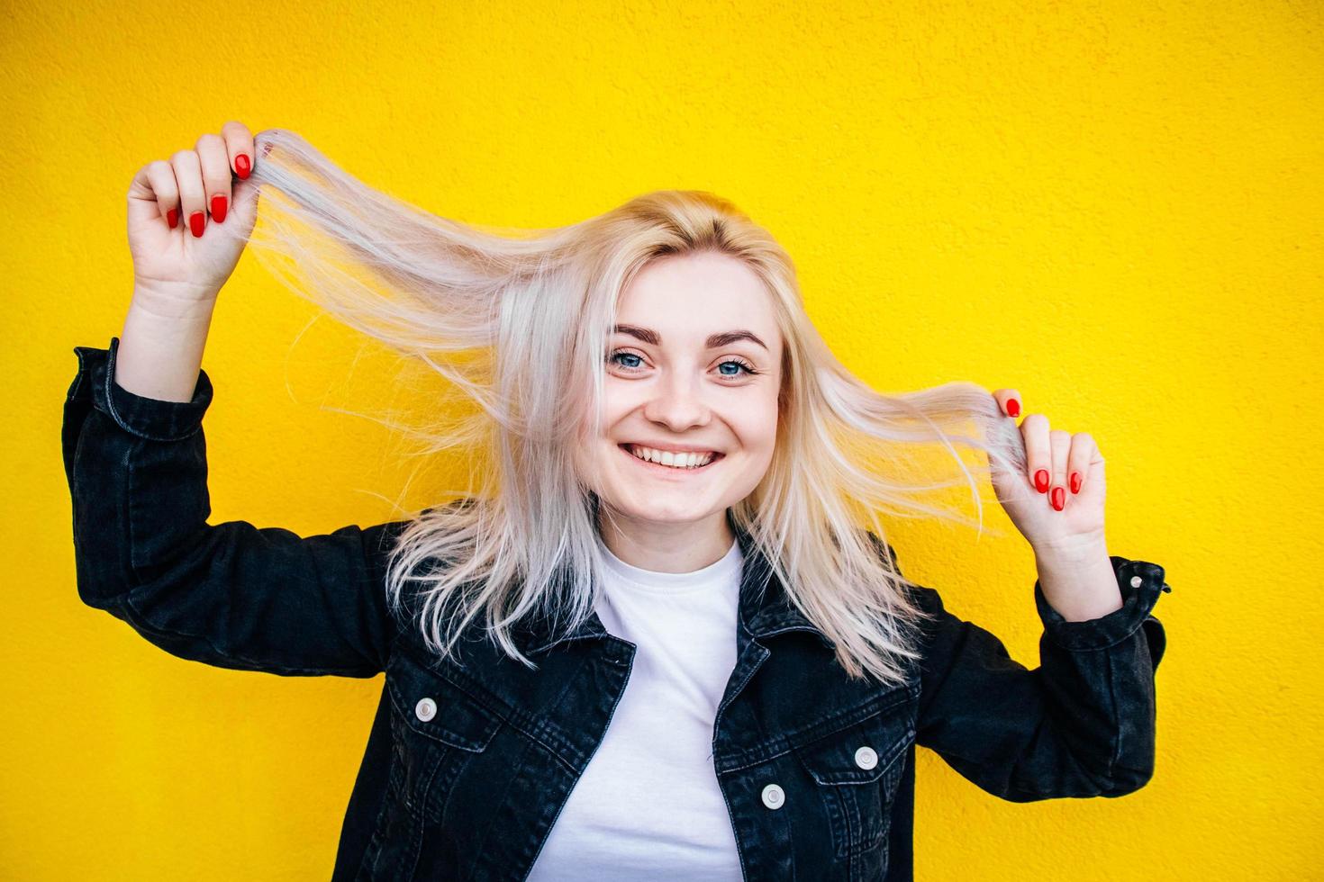 Mujer sonriendo y sosteniendo su cabello sobre fondo amarillo foto