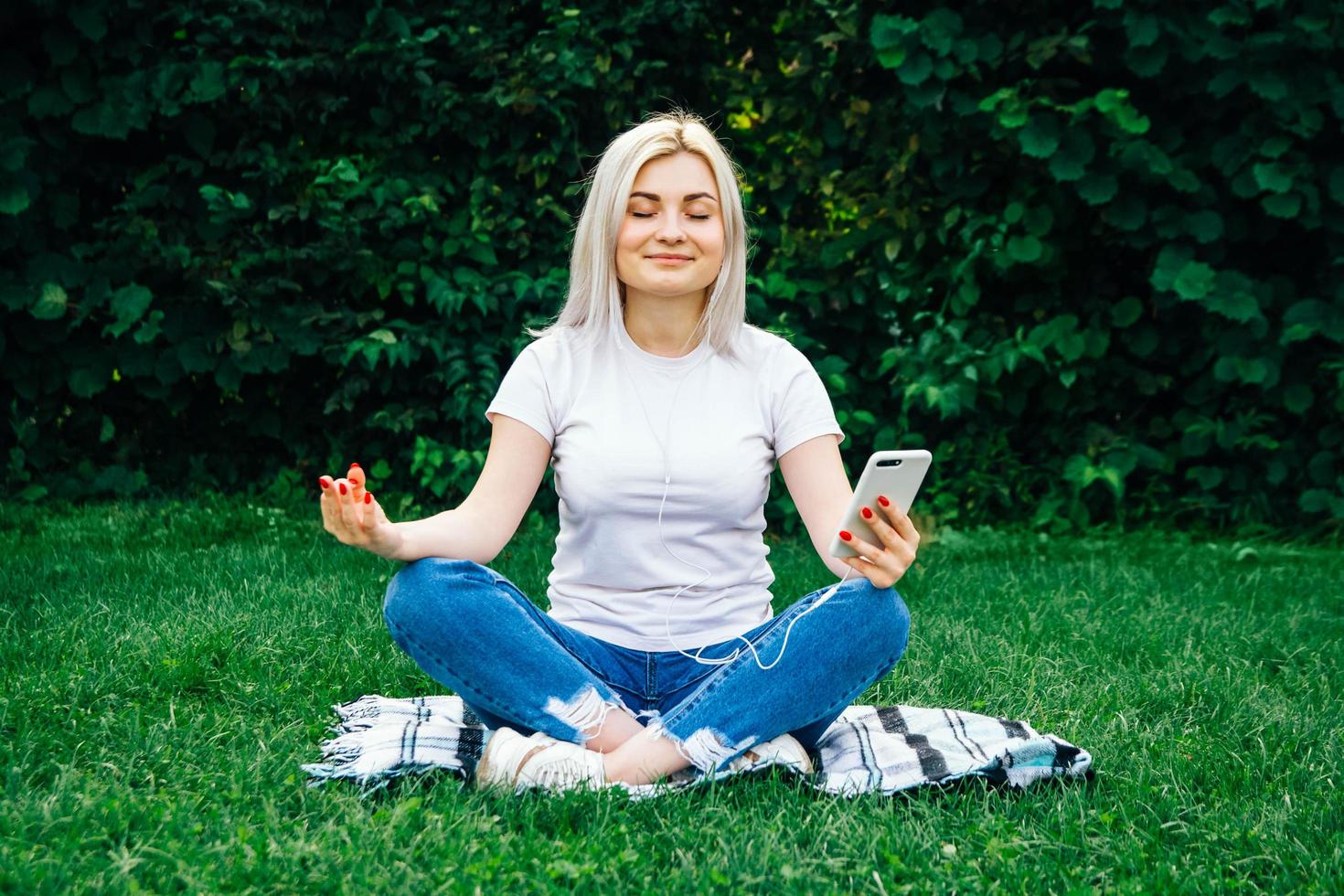 Woman in headphones and smartphone in hands on green grass photo