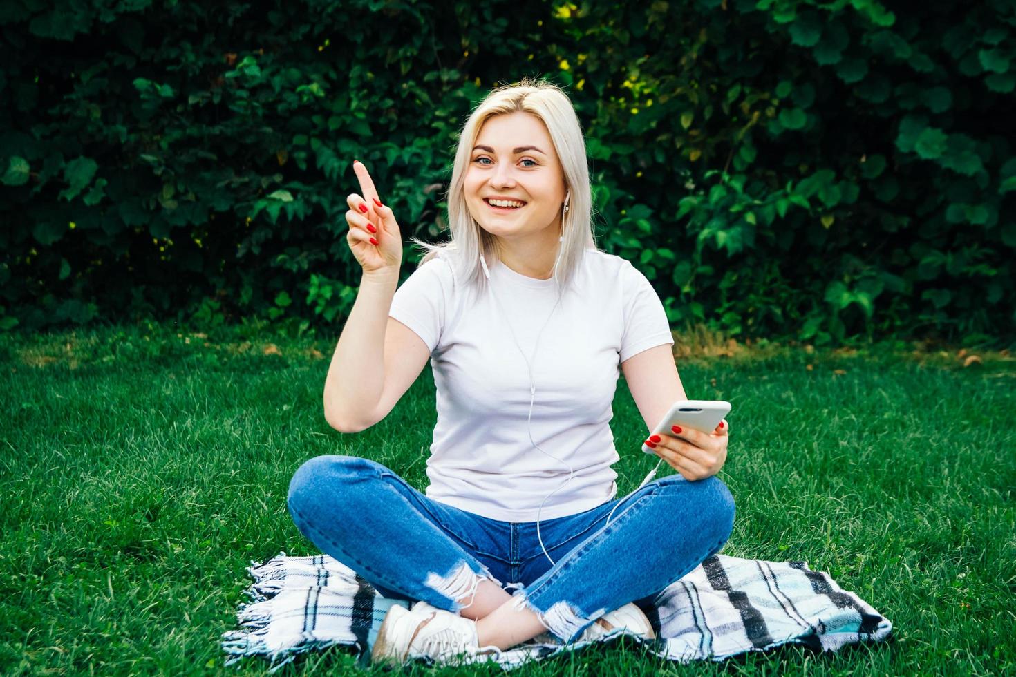 Woman in headphones and smartphone in hands on green grass photo