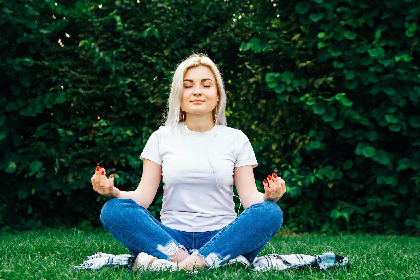 Woman in headphones sits in meditative pose on green grass photo