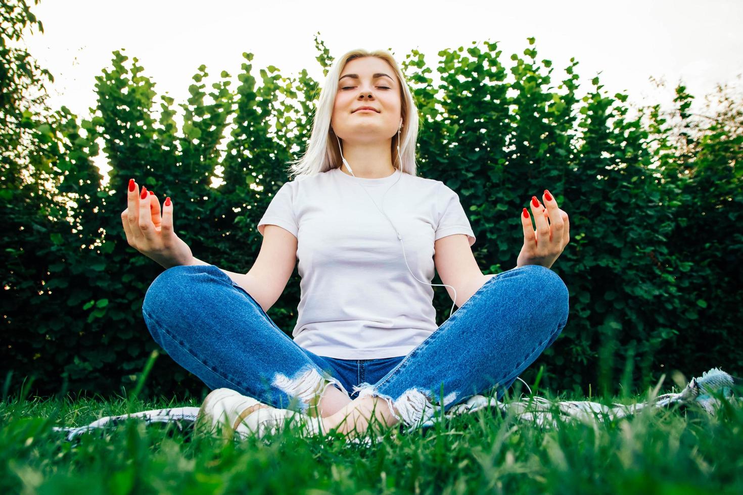 Woman in headphones sits in meditative pose on green grass photo