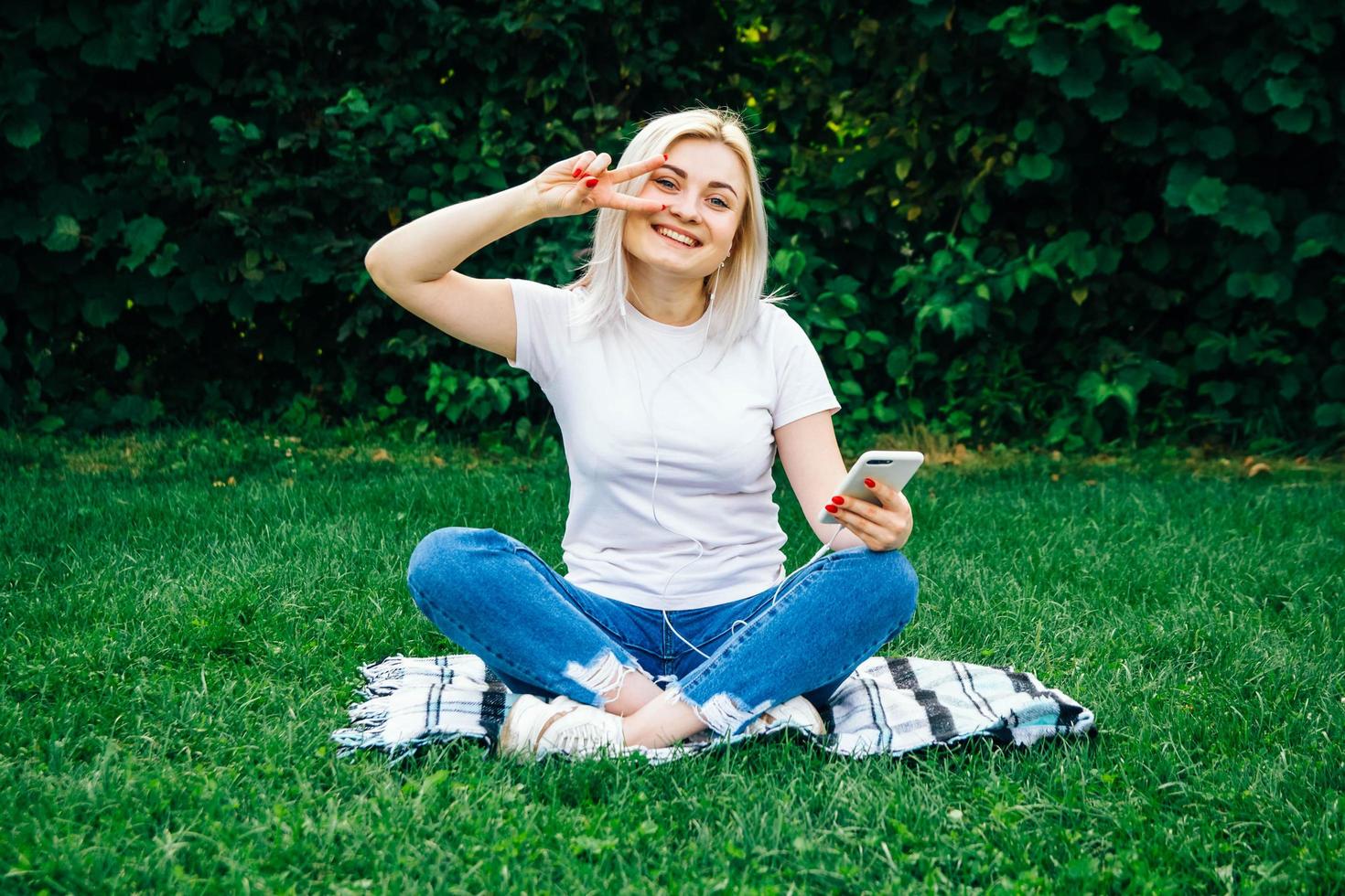 Woman in headphones and smartphone in hands sits on green grass photo