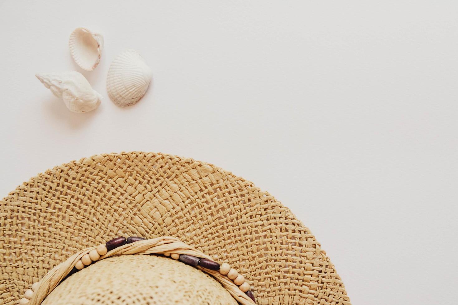 Sombrero de paja y conchas marinas sobre un fondo blanco. foto