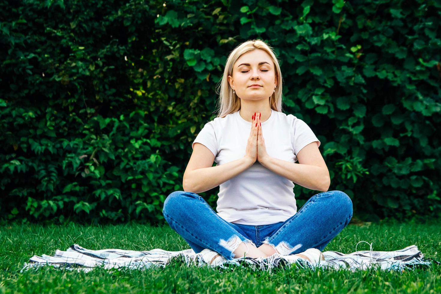 Woman sitting on plaid in meditation pose on green grass photo