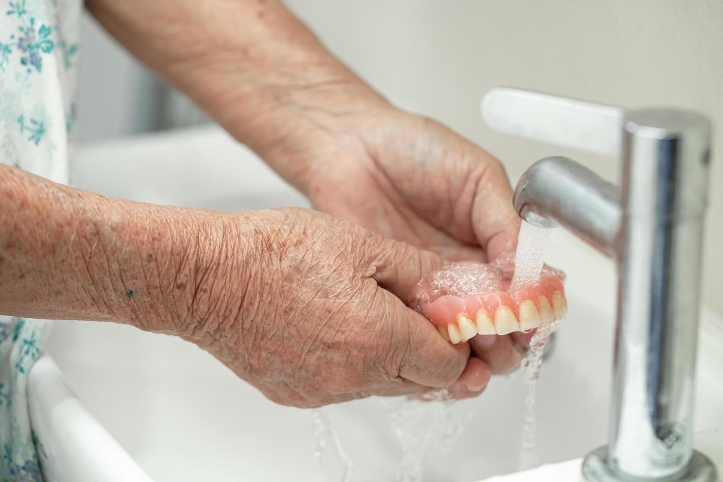 Asian senior woman patient holding and washing denture in nursing hospital ward photo