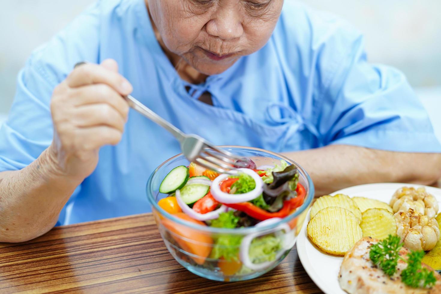 Asian senior or elderly old lady woman patient eating breakfast vegetable healthy food with hope and happy while sitting and hungry on bed in hospital. photo