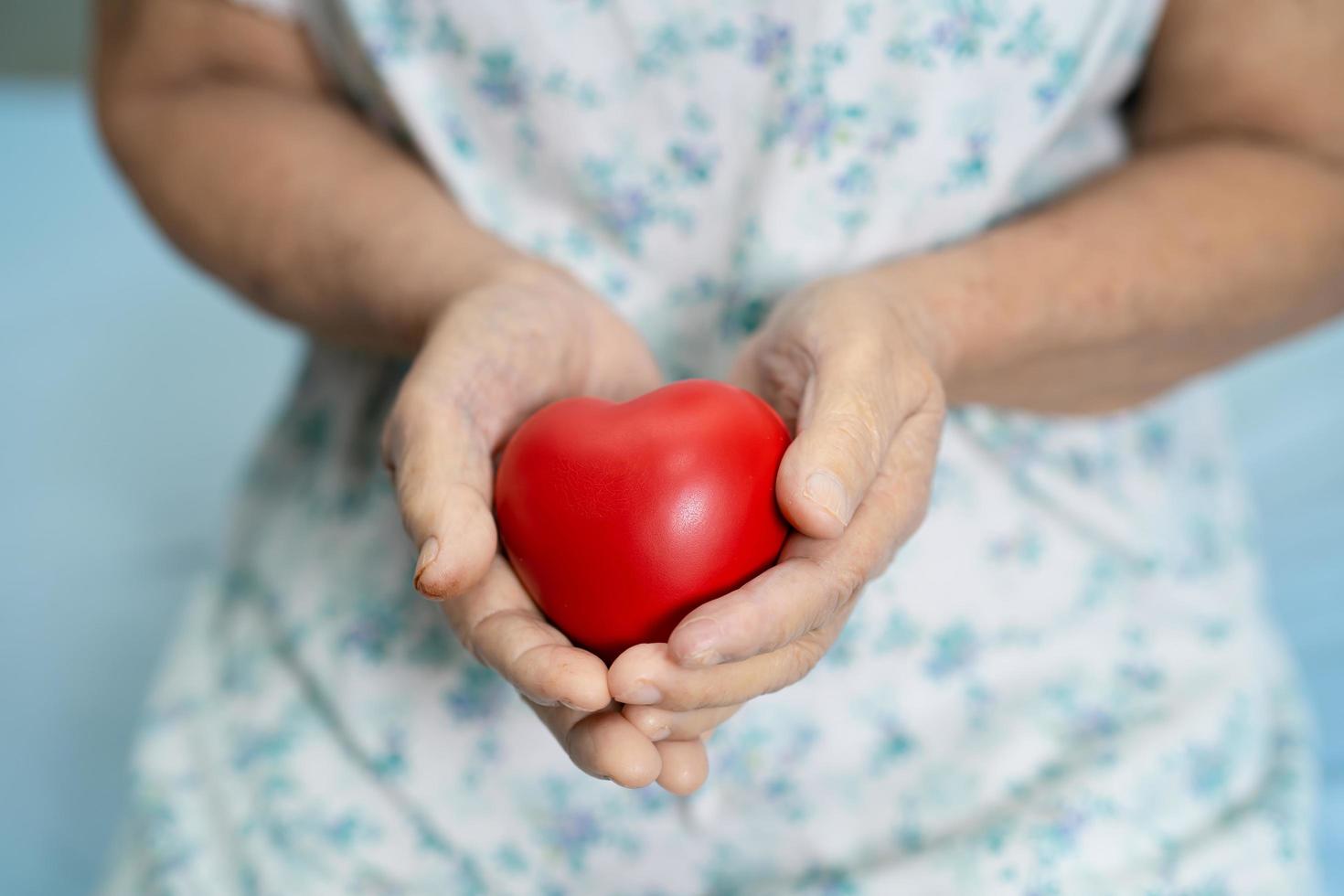 Paciente asiático mayor o anciano mujer sosteniendo un corazón rojo en su mano en la cama en la sala del hospital de enfermería, concepto médico fuerte y saludable foto