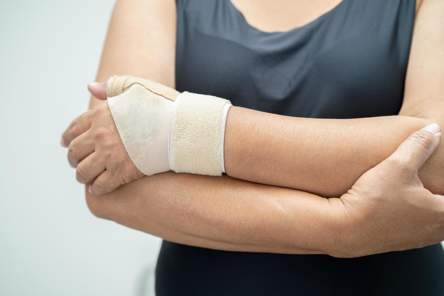 Asian middle-aged lady woman use elastic bandage to treating De Quervain syndrome at hand and finger in office. photo
