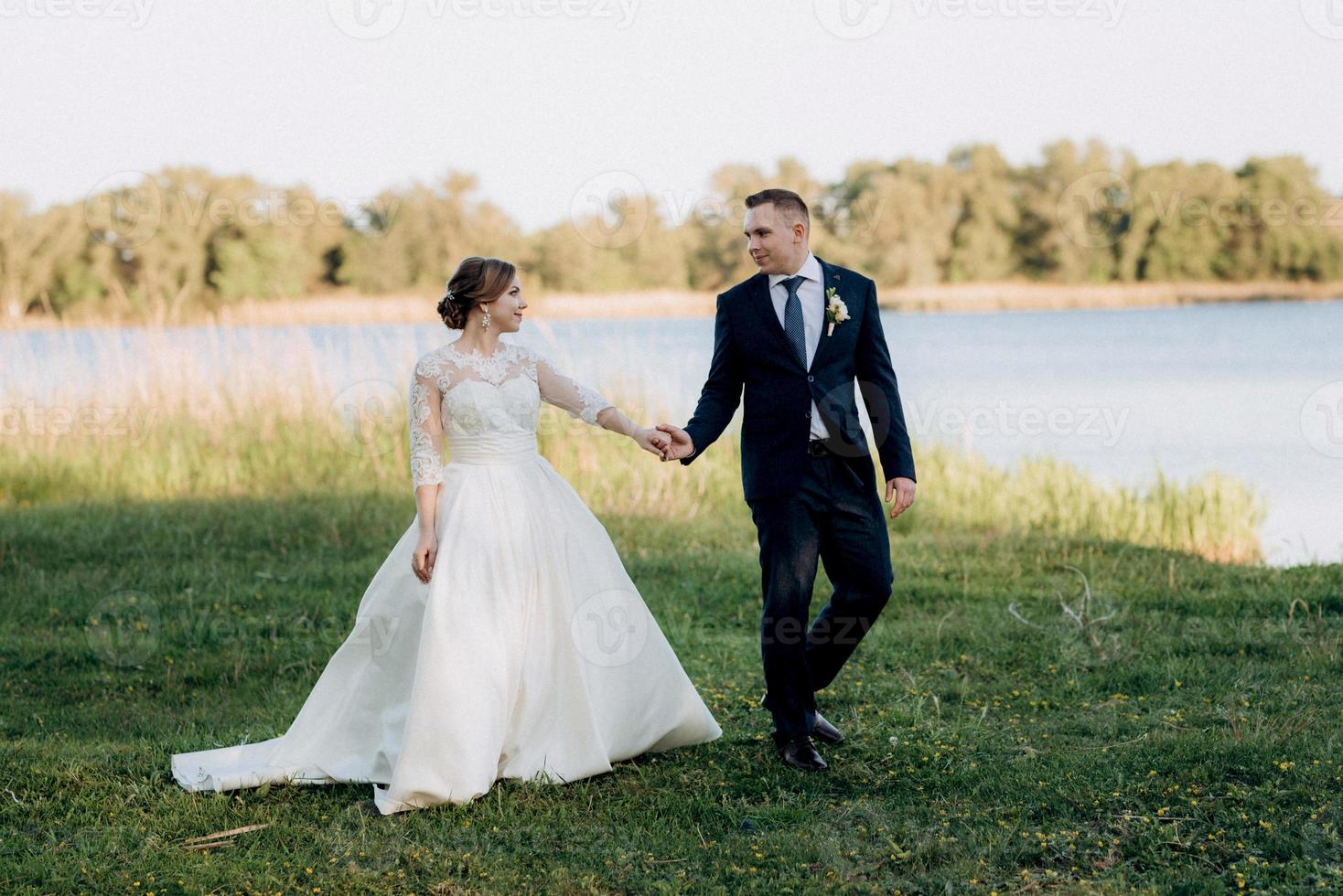 the groom and the bride are walking in the forest near a narrow river photo