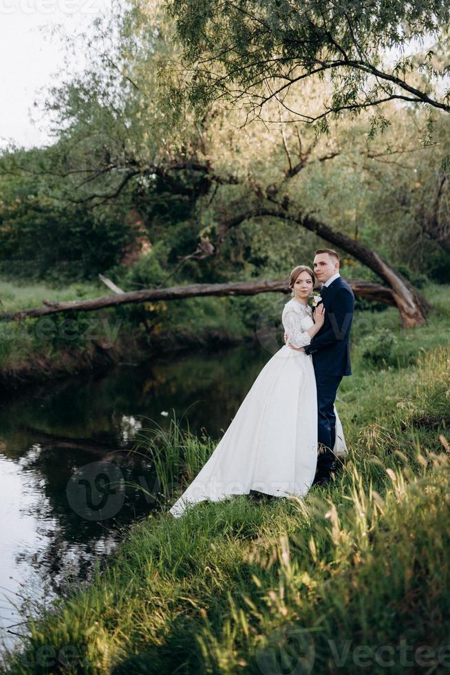 the groom and the bride are walking in the forest near a narrow river photo