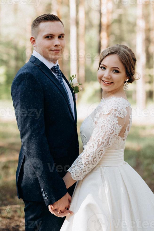 the bride and groom are walking in a pine forest photo