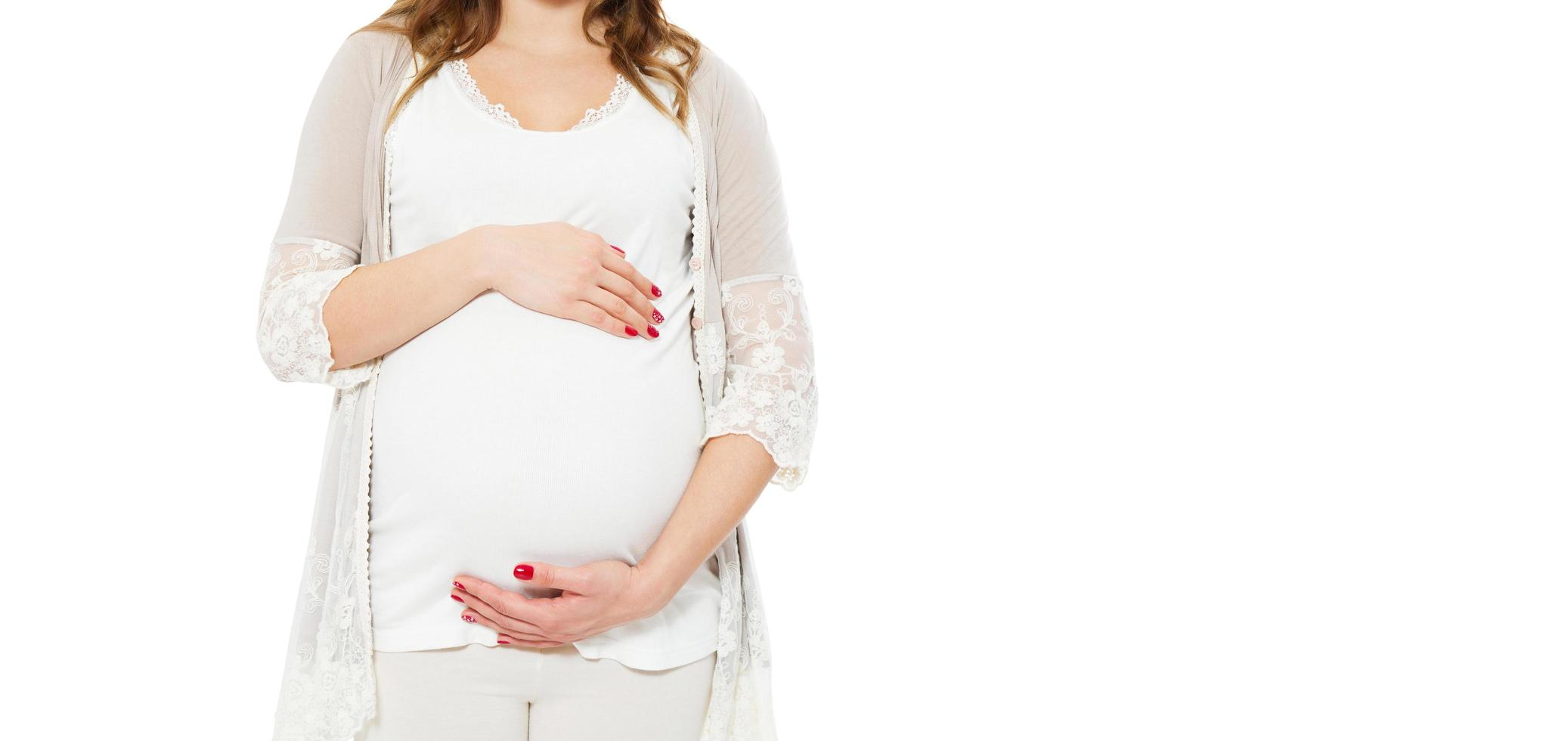 Pregnant woman holds hands on belly on a white background. Pregnancy, maternity, preparation and expectation concept. Close-up, copy space, indoors. Beautiful tender mood photo of pregnancy.