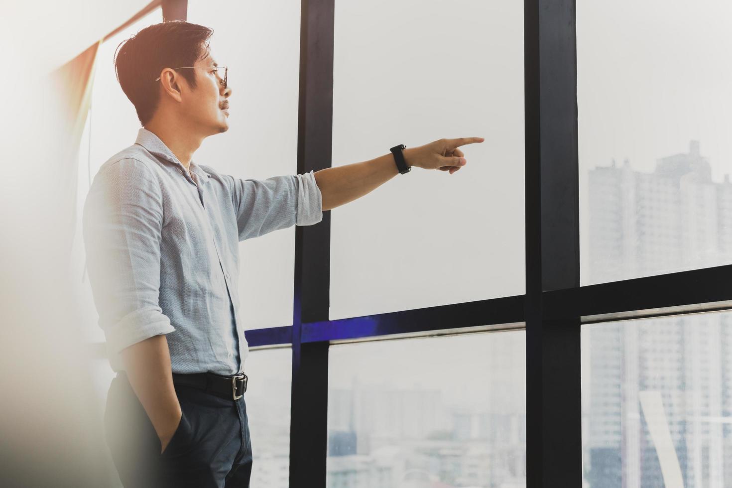 Businessman standing in front of window with hand pointing outside. photo