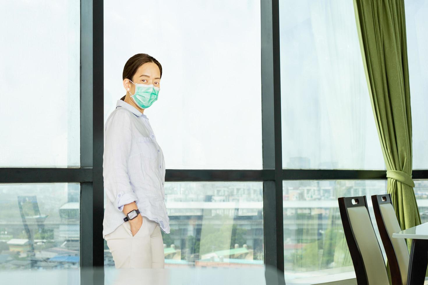 Woman in protective mask standing next to the big window in office. photo