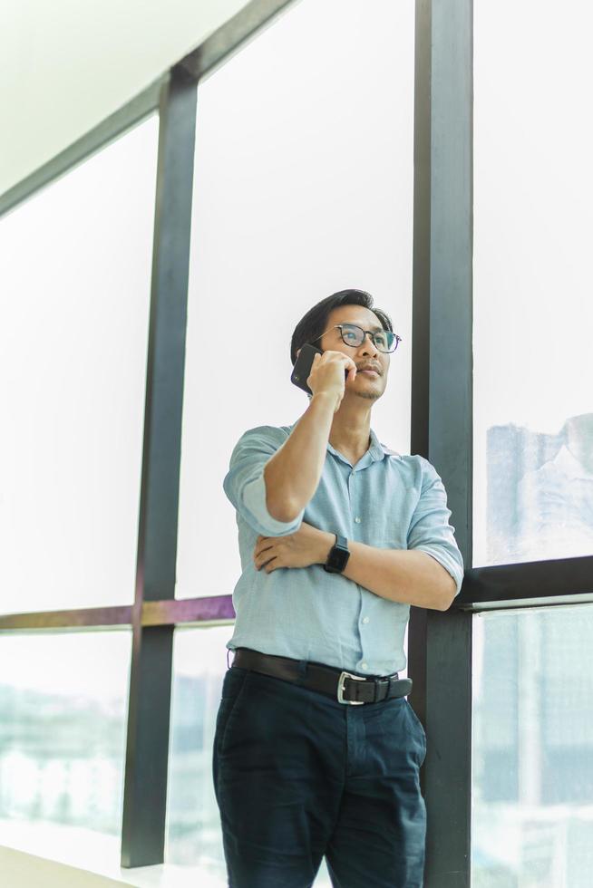 Businessman standing next to big window inside modern building talking  on cell phone. photo